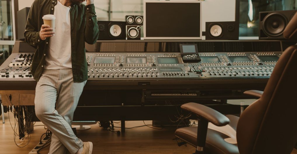 young sound producer standing at studio with cup of coffee to go young sound producer standing at studio with cup of coffee to go
